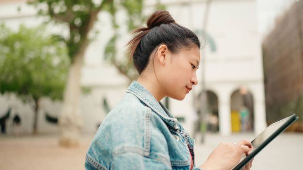 Fiatal lány diák keres információt tabletta pc szabadban. Gyönyörű ázsiai lány öltözött alkalmi tanulás az egyetemi campus - Fotó, kép