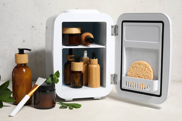 Petit réfrigérateur avec cosmétiques naturels, brosse et feuilles de plantes sur fond clair - Photo, image