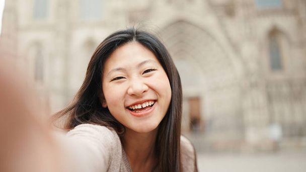 古い建築を背景に自撮りをしながら、アジアの美少女は誠実に笑顔。幸せそうに新しい街を探索する日本人女性 - 写真・画像