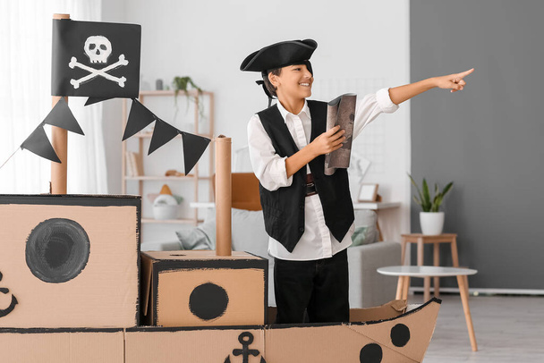 Kleiner Junge im Piratenkostüm spielt zu Hause mit Karte und Pappschiff - Foto, Bild