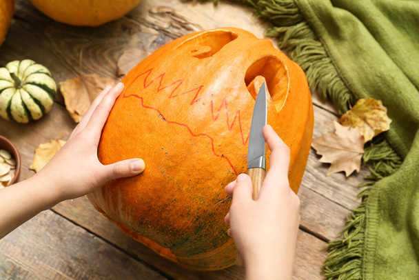 Woman carving Jack-O-Lantern pumpkin on wooden background, closeup - Foto, imagen
