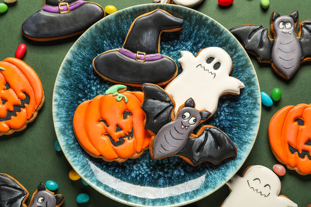 Bowl with Halloween cookies and candies on green background, closeup - 写真・画像
