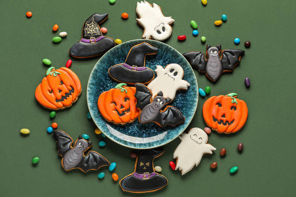 Bowl with Halloween cookies and candies on green background - Foto, afbeelding