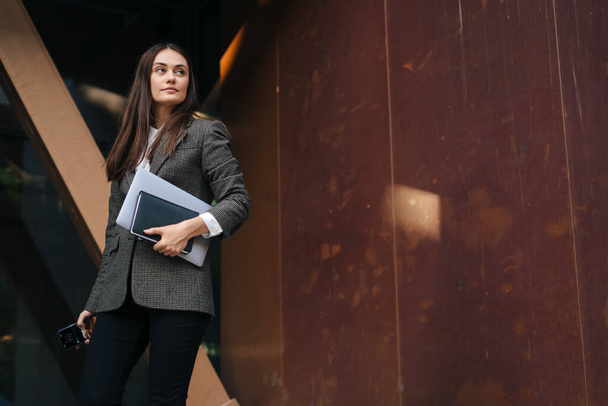 Caucasian businesswoman person standing on street near office building holding laptop dressed in formal wear. Beautiful young girl. Attractive elegant woman - Foto, afbeelding