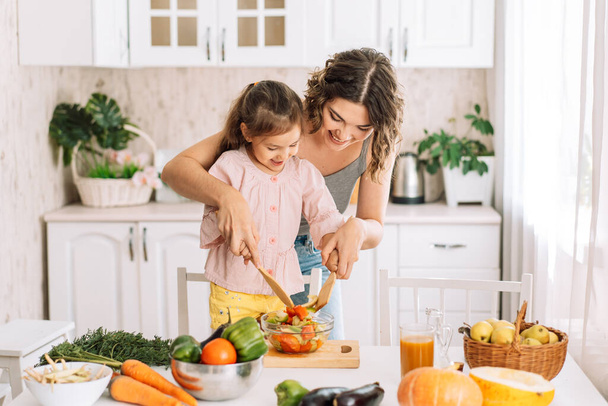 Mom and daughter are mixing salad together with wooden spatulas. - Φωτογραφία, εικόνα