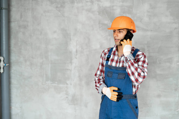 Jovem muçulmano ou construtor no capacete com prancheta chamando no smartphone sobre fundo de parede de concreto cinza. conceito de reparação, construção, construção, negócios e manutenção - Foto, Imagem