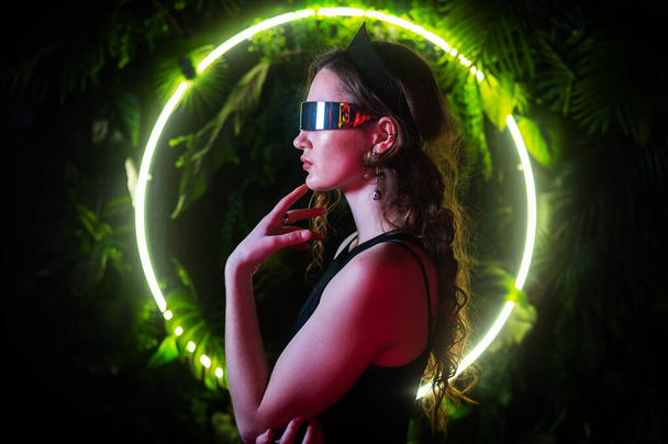 Caucasian woman in panoramic sunglasses against the background of an annular neon lamp in plants - Zdjęcie, obraz
