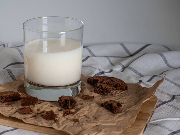 Склянка молока та печива з какао та зі шматочками шоколаду всередині на папері для випічки на білому тлі. Сніданок їсть. Копіювати простір
 - Фото, зображення