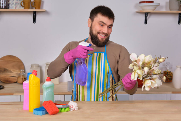 Image d'un jeune homme barbu caucasien dans la cuisine, il fait peu de présentation de tous ses détergents, se préparant à un grand nettoyage. Homme prenant soin des fleurs
 - Photo, image