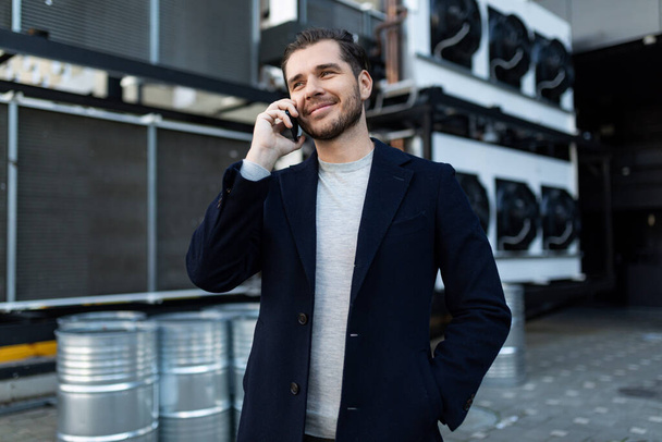 Erkek girişimci endüstriyel bir geçmişe karşı cep telefonuyla konuşuyor. - Fotoğraf, Görsel