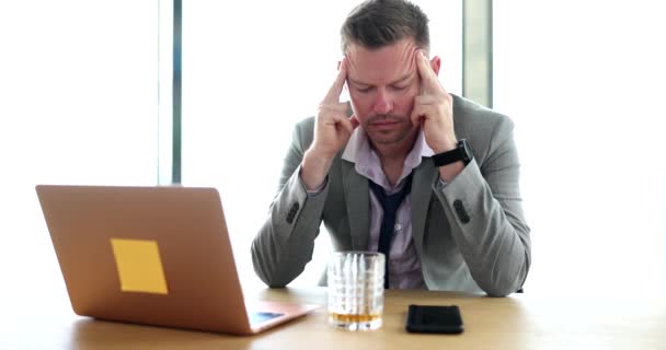Hombre de negocios cansado masajeando su cabeza en la mesa con un vaso de whisky 4k película cámara lenta. Situación estresante en el concepto de trabajo - Imágenes, Vídeo
