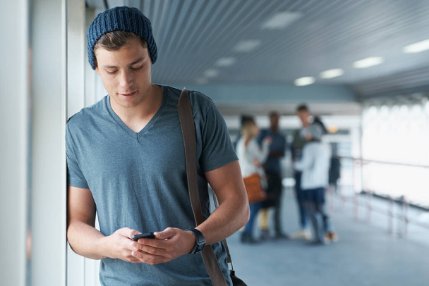 Jeho mobil je jeho sociální síť. pohledný mladý student vysoké školy drží mobilní telefon s přáteli v pozadí - Fotografie, Obrázek