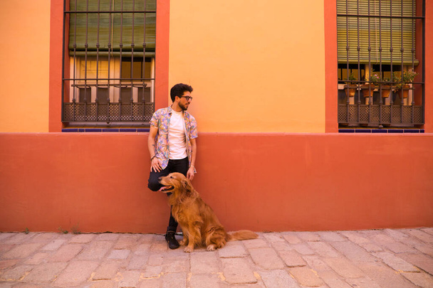 молодий латинський чоловік і його коричневий золотий собака-ретривер, чоловік встає дивиться на свого улюбленця, який сидить на землі і хапає голову. Концепція домашніх тварин
. - Фото, зображення