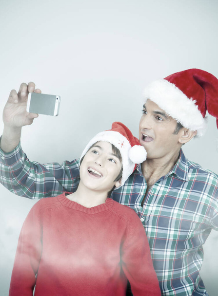 Happy smiling father and son wearing Christmas hat taking selfies on a white background - Photo, Image