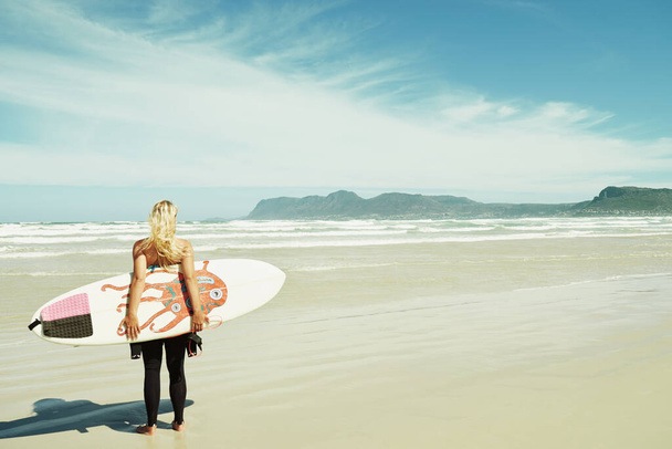En route vers l'océan. Une jeune surfeuse tenant sa planche de surf debout sur une plage - Photo, image