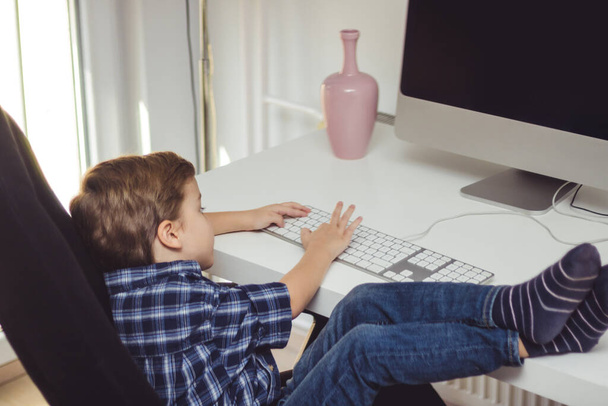 Kleiner Junge mit Füßen auf dem Tisch mit dem Computer zu Hause. - Foto, Bild