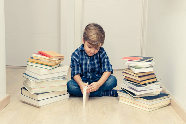 Маленький ребенок учится, сидя на полу среди кучи книг.  - Фото, изображение