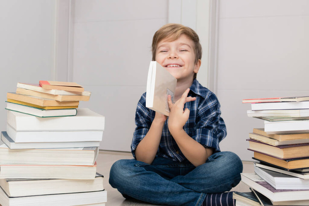 Gelukkig kind zittend tussen stapels boeken en kijkend naar camera.  - Foto, afbeelding