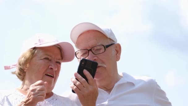 I pensionati americani si rilassano nel parco, usando uno smartphone e divertendosi. Felice nonni - Filmati, video
