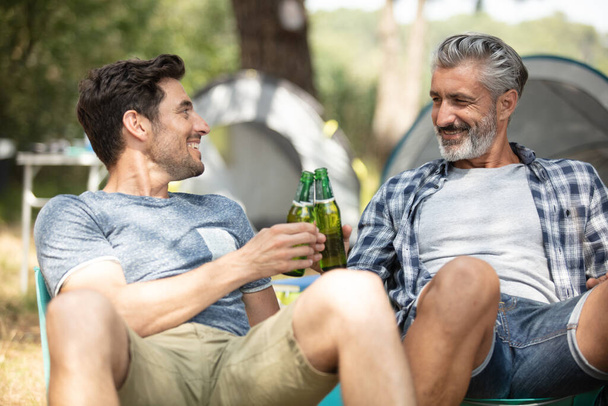 male friends sitting on chairs talking drinking beer - Foto, Imagen