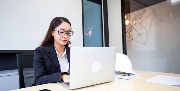 Ασιάτισσα επιχειρηματίας που χρησιμοποιεί φορητό υπολογιστή για εργασία και κάνει έρευνα στο διαδίκτυο στο γραφείο της. - Φωτογραφία, εικόνα