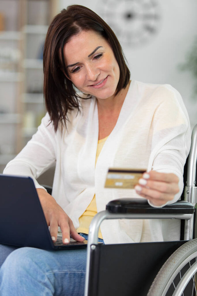 Nette Seniorin im Rollstuhl tippt Kartennummer auf Laptop - Foto, Bild