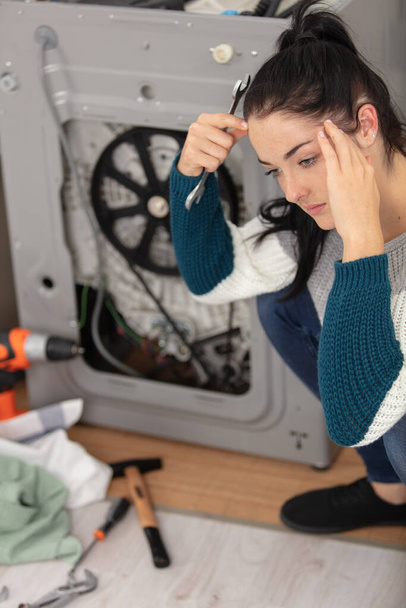 depressed woman with spanner next to broken washing machine - Foto, Imagen