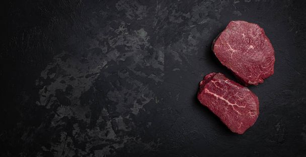 Two fresh raw beef steaks with spices ready to cook on a dark background. Long banner format. top view, - Zdjęcie, obraz