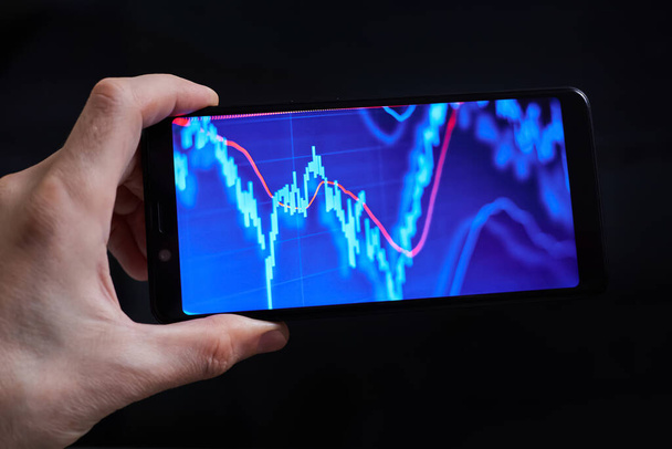 Trader analyzes stock market data in smartphone on dark background - Photo, Image