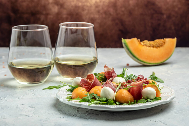 Cantaloupe melon with prosciutto or jamon and green basil leaves with glass of wine. delicious superfood salad, Traditional Italian snack antipasti. place for text, - Foto, Imagen