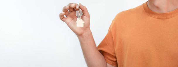 Banner of young man with the new home keys. Keychain in the shape of a wooden house on white background. High quality photo - Foto, imagen