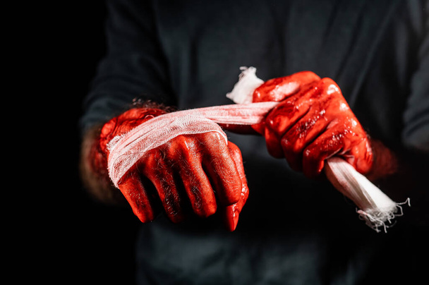 A man covered in blood bandages his hands - Foto, afbeelding