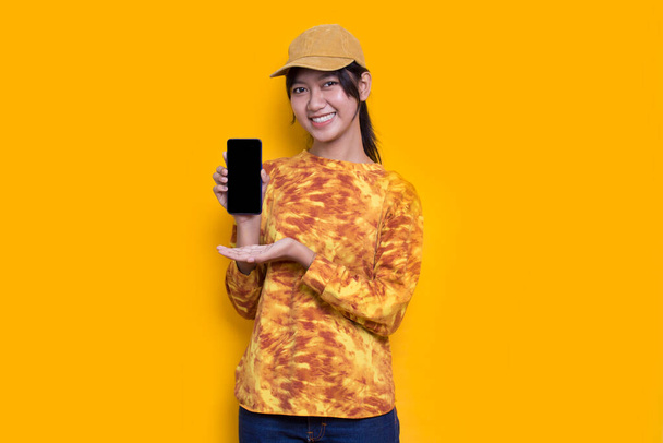 young beautiful asian woman demonstrating mobile cell phone isolated on yellow background - Photo, Image