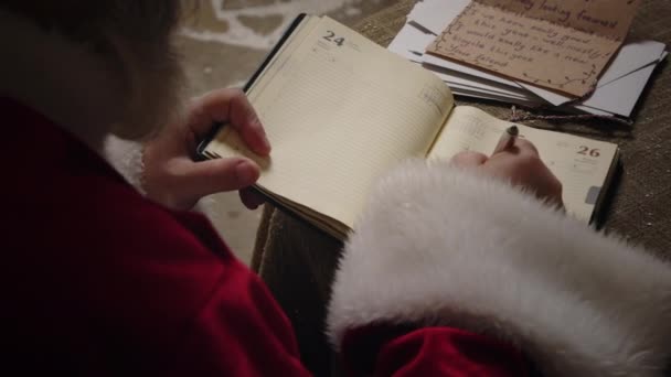 Papá Noel está trabajando en su residencia, Polo Norte, haciendo una lista de regalos, escribiendo en su planificador, tratando con cartas recibidas de todo el mundo, cámara lenta. - Metraje, vídeo