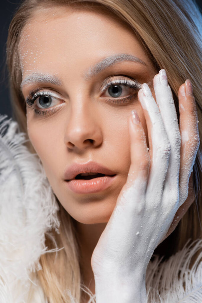 portrait of young blonde woman with winter makeup touching face with hand in white paint - Φωτογραφία, εικόνα