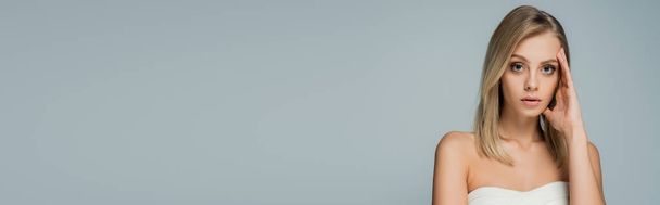συμπυκνωμένη γυναίκα με γυμνούς ώμους και φυσικό μακιγιάζ κοιτάζοντας κάμερα απομονωμένη σε γκρι, banner - Φωτογραφία, εικόνα