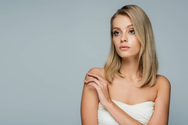 blonde woman with bare shoulders and natural makeup looking away isolated on grey - Photo, Image