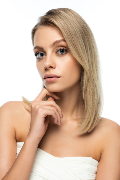 portrait of blonde woman with blue eyes looking at camera while touching face isolated on white - Photo, Image