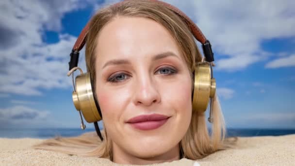 Uma mulher bonita enterrada na cabeça em uma praia ouvindo música em fones de ouvido - Filmagem, Vídeo