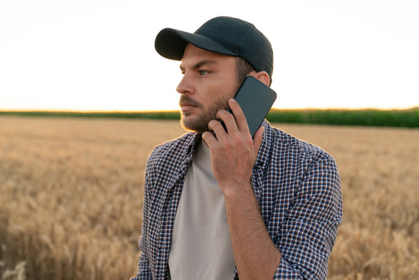 Bearded farmer with mobile phone and digital tablet in agricultural field at sunset  - Foto, Imagem