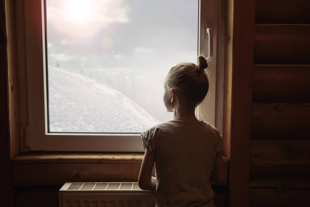 Seikkailun jano. Pieni tyttö seisoo lähellä ikkunaa ja katselee sivuun ja nauttii aurinkoinen päivä. Ole hyvä. - Valokuva, kuva
