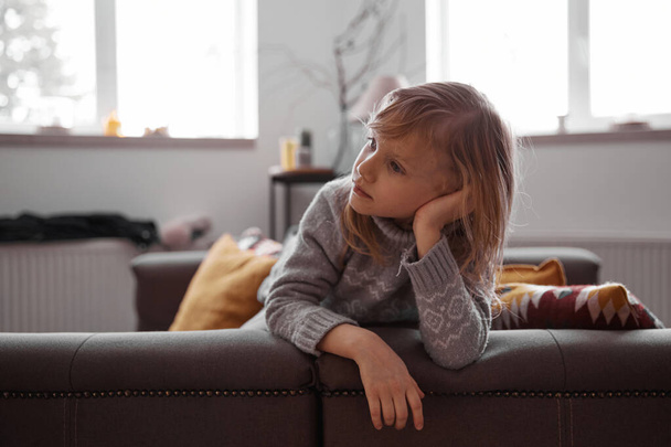Mooi klein meisje zitten op gezelligheid bank in de woonkamer thuis en tv kijken - Foto, afbeelding