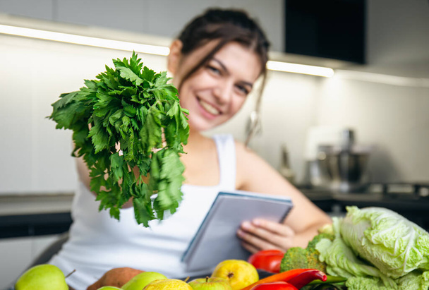 Una joven en la cocina con un cuaderno y verduras, el concepto de cocina, dieta y salud. - Foto, Imagen
