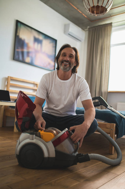 Housework. Man sitting on the floor and gathering the vacuum cleaner - 写真・画像