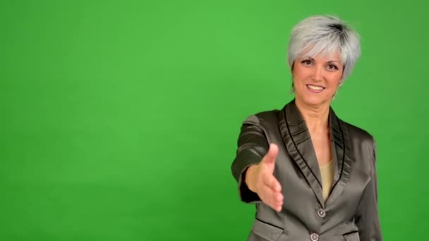 Business middle aged woman gives a hand in greeting and smiles - green screen - studio - Footage, Video