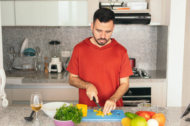 Az ember zöldségeket aprít a vágódeszkán, miközben egészséges ételt készít az otthoni konyhájában. - Fotó, kép