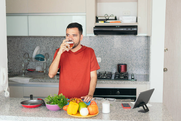 muž popíjí pivo, zatímco připravuje jídlo ve své domácí kuchyni - Fotografie, Obrázek
