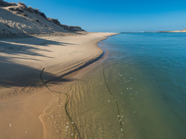 ヴィラ・ノヴァ・デ・ミルフォンテス、ビセンティーヌ・コースト自然公園ポルトガルでミラ川のターコイズブルーの水とプライア・ダス・ファールナス黄金の砂のビーチの眺め。晴れた日青い空. - 写真・画像