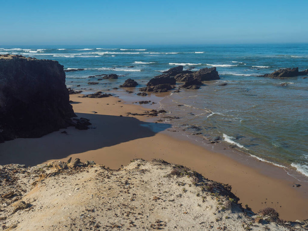 Veduta di Praia das Furnas spiaggia di sabbia dorata con onde oceaniche e rocce taglienti e scogliere nella selvaggia costa di Rota Vicentina vicino a Vila Nova de Milfontes, Portogallo - Foto, immagini