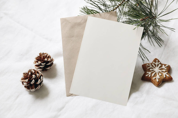Christmas still life. Empty greeting card, invitation mockup. Gingerbread cookie, pine cones and pine tree branches on white linen tablecloth in sunlight. Gift wrapping concept, winter festive flatlay - Fotó, kép